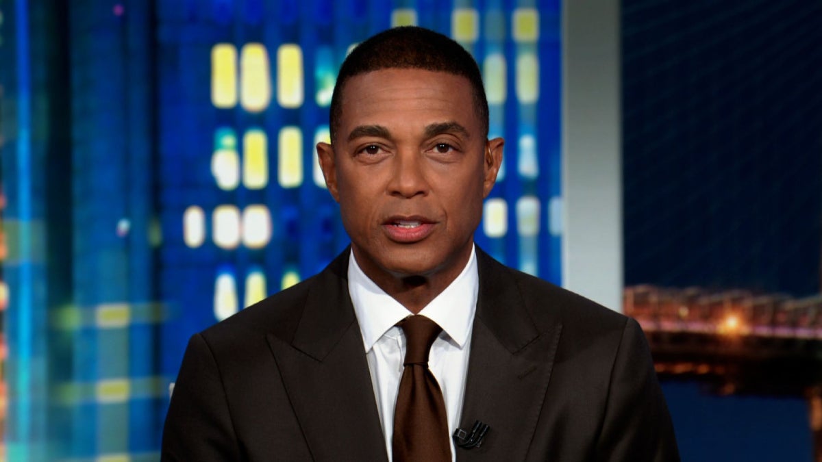 CNN Don Lemon Crime Jennings 8 - A man wearing a dark suit, white shirt, and brown tie sits in a television studio with a colorful blue and yellow background featuring illuminated windows and a cityscape. He appears to be participating in a news broadcast or interview. The atmosphere is professional and serious. No visible text in the image.