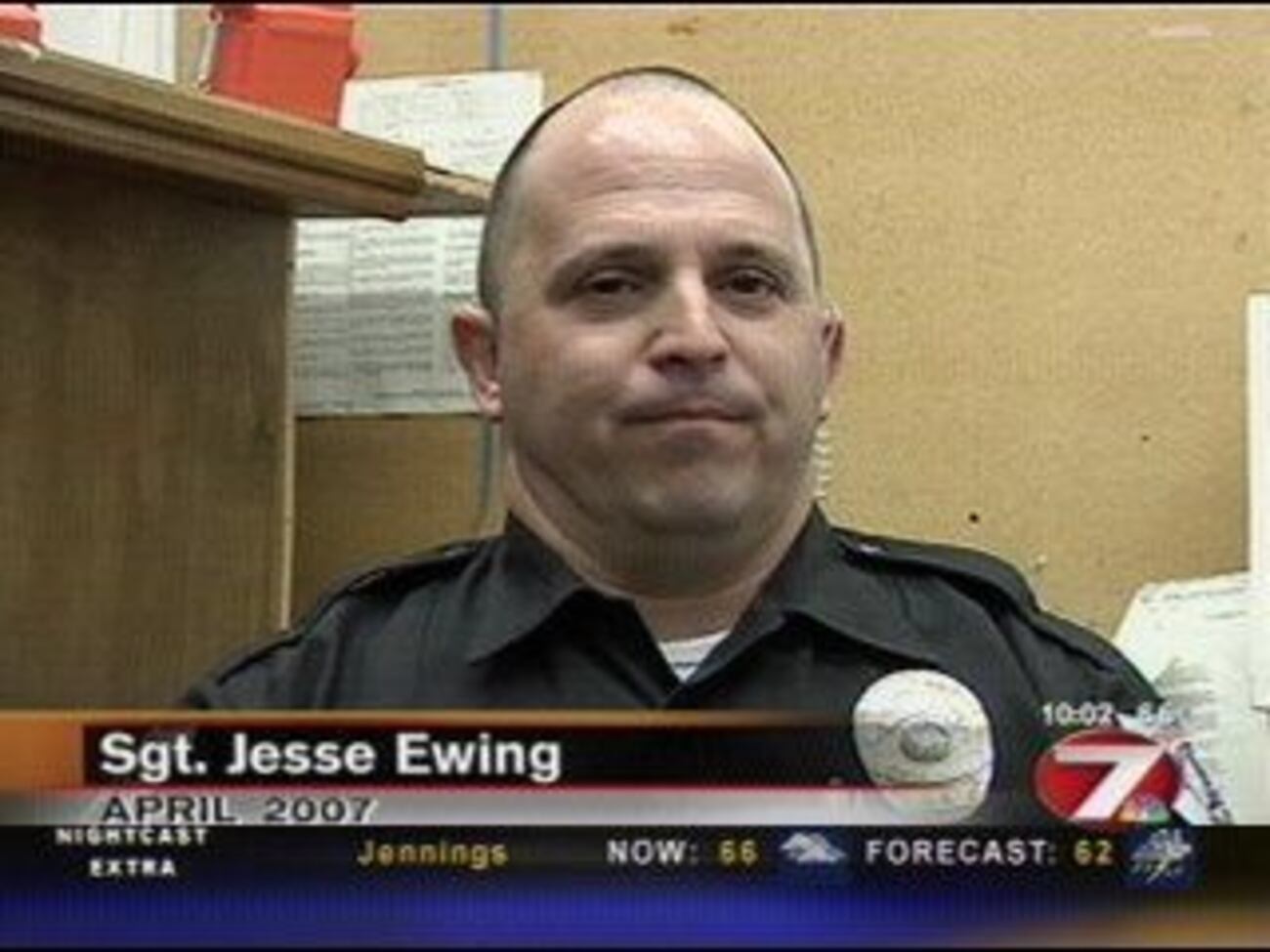 A police officer in uniform stands in an office environment with bulletin boards and paperwork in the background. On-screen text reads Sgt. Jesse Ewing, April 2007, and includes a news ticker with weather and forecast information. The emotional tone is serious and professional, reflecting a news interview or report setting.